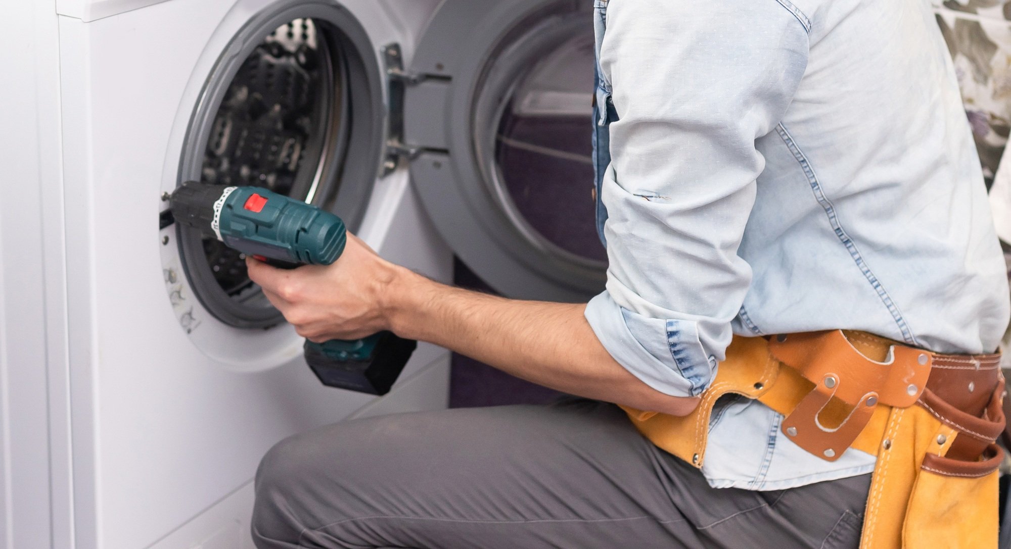 Young handyman fixing washing machine, closeup. Laundry day.