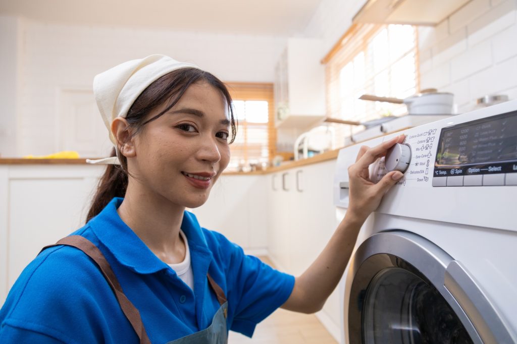 Young housewife doing laundry, drying, spinning with automatic washing machine.