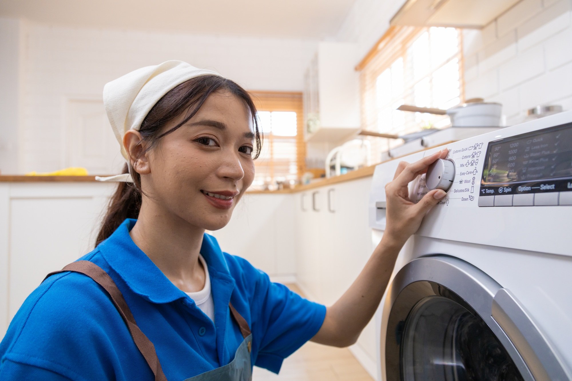 Young housewife doing laundry, drying, spinning with automatic washing machine.