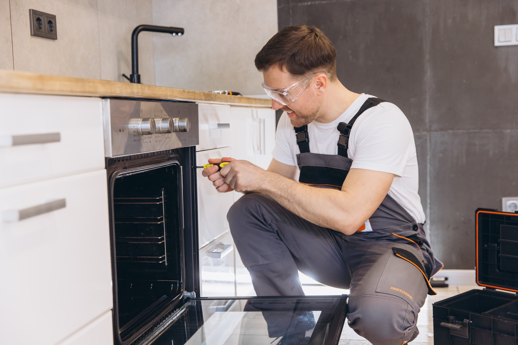 Professional plumber repairing oven in a modern kitchen